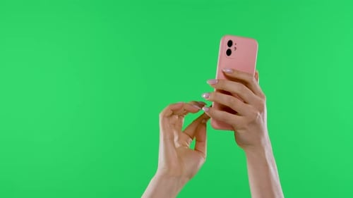 Female Hands Hold the Smartphone Vertically Against the Background of the Green Screen of the Chroma