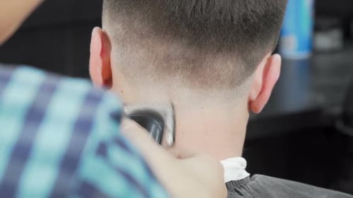 Sliding Rear View Shot of a Barber Using a Clipper Giving a Haircut To Male Client