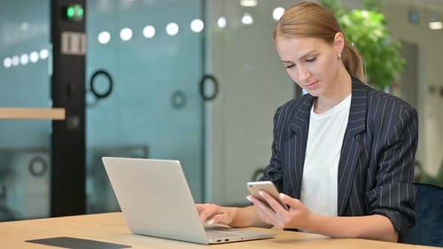 Woman Using Laptop and Smartphone in Office
