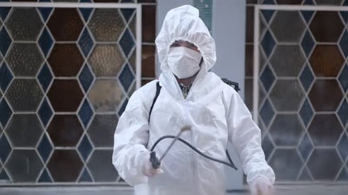 Zivilschutzteam in Schutzkleidung desinfiziert Arbeitsplätze als Coronavirus-Maßnahme (Covid-19)