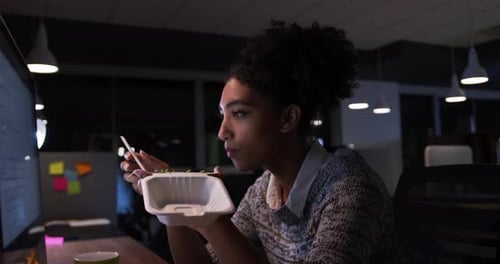 Businesswoman working and eating in a modern office by night