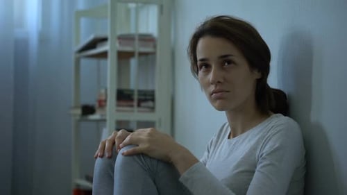 Distressed Woman Sitting Against Wall in Room