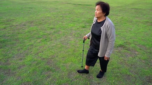slow-moiton of senior woman walking with walking stick in the grass field