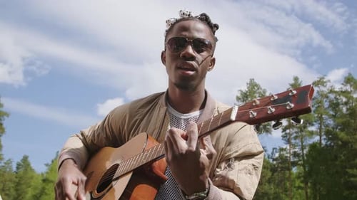 Man Playing Acoustic Guitar Outdoors in a Forest