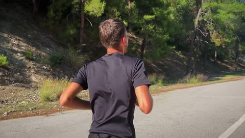 Man Jogging on Road Along a Forested Hillside