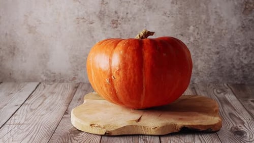 Nahaufnahme eines großen orangefarbenen Kürbises auf Holzbrett und rustikalem Hintergrund