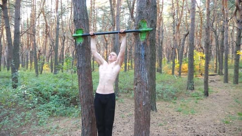 Starker und muskulöser Mann macht Klimmzüge im schönen Wald. Männlicher Sportler beim Training auf horizontaler Ebene