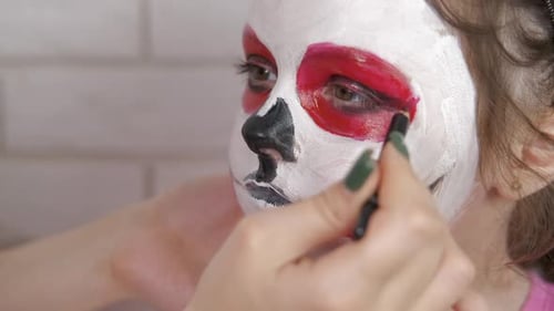 Little girl paints paint face. Halloween.