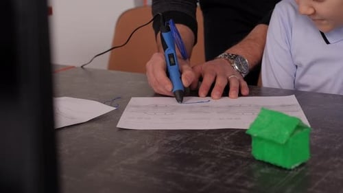 A Young Man Teaches a Student Boy to Draw with a 3D Pen in a Robotics School