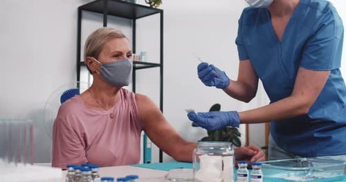 Beautiful Senior Caucasian Woman Gets Vaccinated By Young Doctor in Blue Scrubs Receives Injection