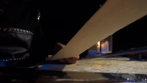 Person Unrolls Ancient Map by Candlelight at Night