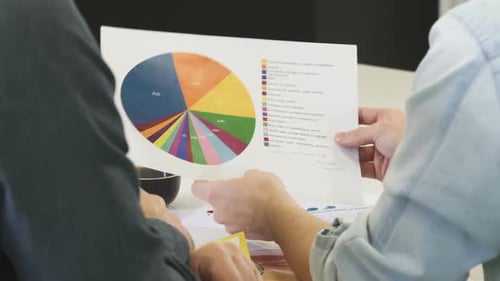 Abgeschnittene Aufnahme von zwei Geschäftsleuten, die über ein gedrucktes Diagramm diskutieren