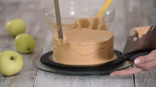 Cake Being Frosted With Caramel Icing On Wooden Table