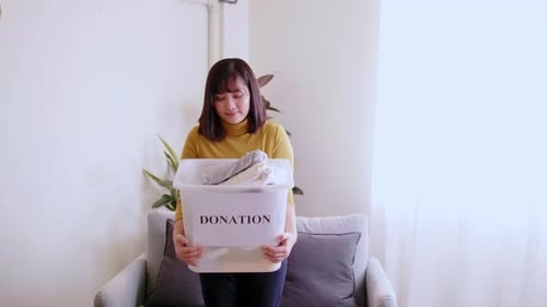 Portrait of young pretty woman looking at camera holding box with clothes for donation. Concept camp