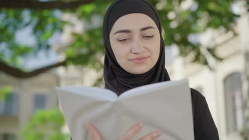 Close-up of Concentrated Muslim Woman Reading Book Outdoors. Absorbed Young Beautiful Lady Enjoying