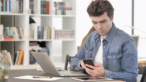 Man with Laptop Using Smartphone at Desk