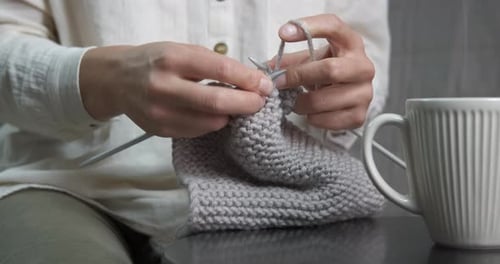 Woman Knitting Grey Yarn Fabric Next to Mug
