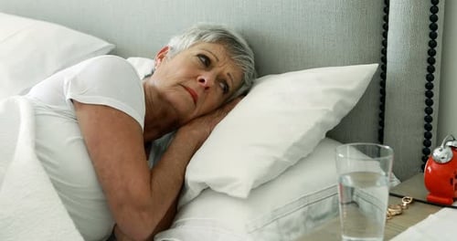 Senior woman turning off alarm clock in bedroom