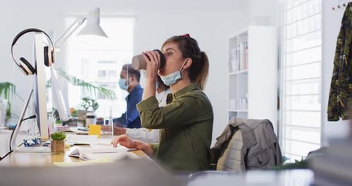 Woman drinking coffee while sitting on her desk at office