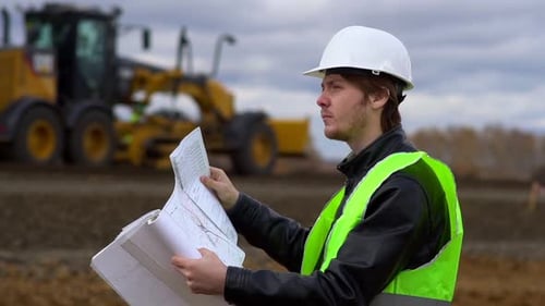 The Worker Looks at the Drawings on the Background of the Road Under Construction