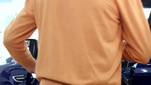 Senior Man Sits Down Into the Car at the Dealership