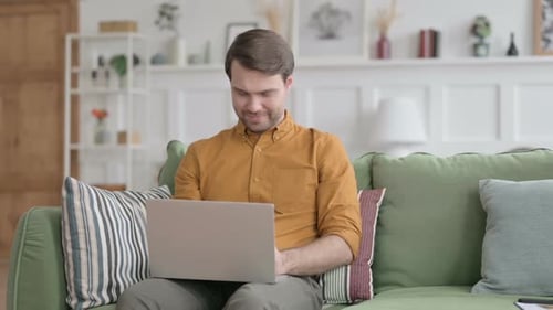 Man Working on Laptop While Sitting on Sofa
