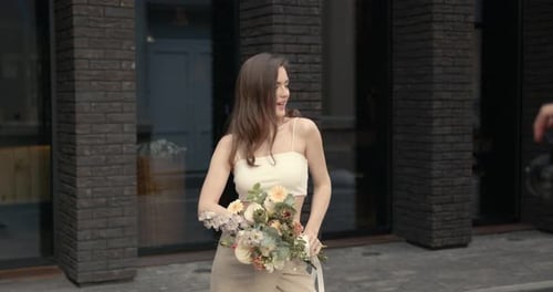 Happy Elegant Young Woman with Flowers in the City