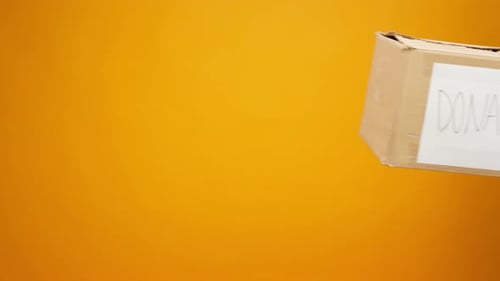 Gloved Hands Holding Donation Box on Yellow Background