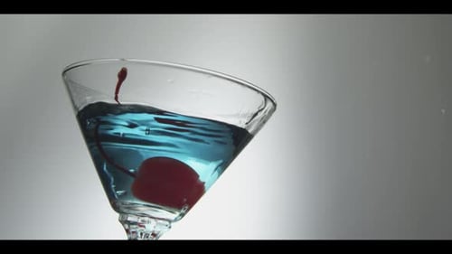 Red Cherry Drops Into Glass With Blue Liquid