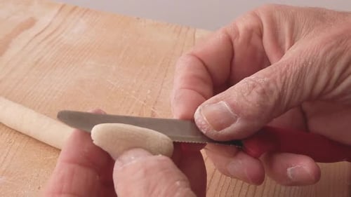 Hands Making Pasta with Knife on Wooden Board