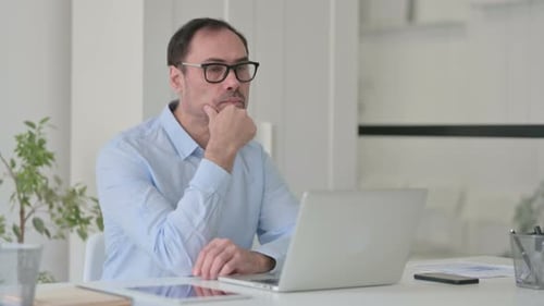 Middle Aged Man Thinking While Using Laptop in Office