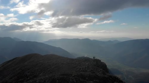 Three people on top of mountain, storm is coming. Aerial shot of people in darkness, revealing storm
