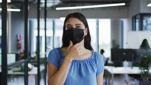 Portrait of caucasian businesswoman adjusting face mask standing in office and looking to camera