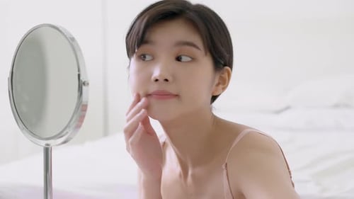 Beautiful young asian woman smiling look at mirror of checking face with skin care and cosmetic.