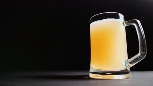 Niedriger Winkel, männlich, von Hand, stellt große Tasse mit frischem Craft Beer auf den Tisch, isoliert auf schwarzem Studiohintergrund