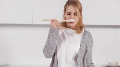 Woman Tasting Food off Wooden Spoon in Kitchen