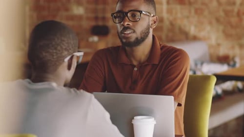 Two Young Men Chatting At Table With Laptop