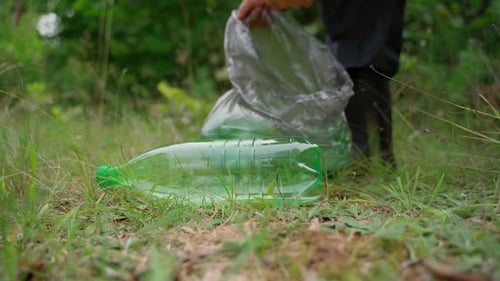 Unrecognizable man cleans up garbage in forest closeup. Male hand remove plastic bottle