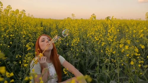 Young Redhair Woman Blowing Bubbles at the Camera Outdoors in Summer Meadow