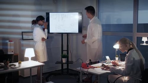 Intelligentes Team von Elektronikentwicklungsingenieuren diskutiert im Labor etwas auf einem großen Fernsehbildschirm