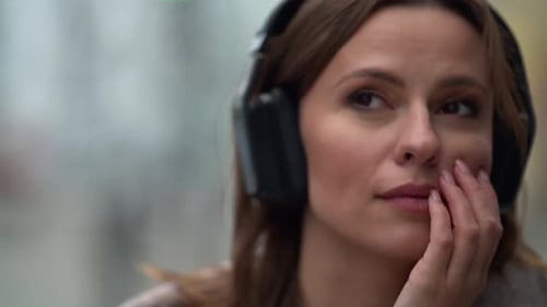 Pensive Woman Is Smiling, Listening To Music By Headphones and Walking in City, Closeup Portrait