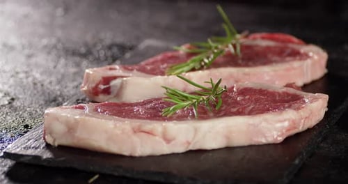 Raw Steak Beef Striploin with Rosemary Rotates on Table.