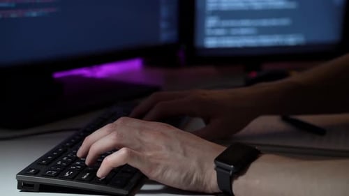 Jovem programador trabalha na frente do computador digitando no teclado e escrevendo notas em macro
