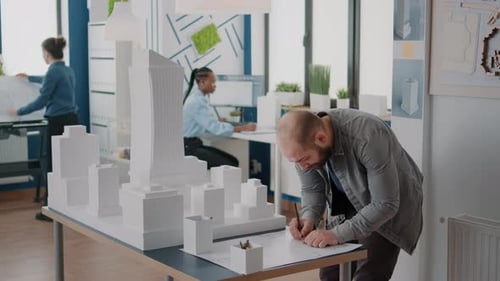 Man Architect Taking Notes on Blueprints Plan to Design Building Structure and Model