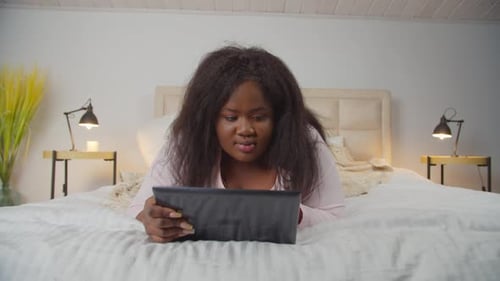 Woman Using Tablet Lying on Bed at Home