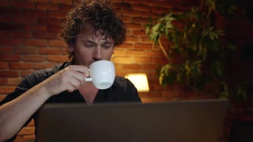 Jeune homme d'affaires prospère buvant du café travaillant au bureau la nuit