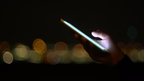Hand Using Cell Phone in City at Night