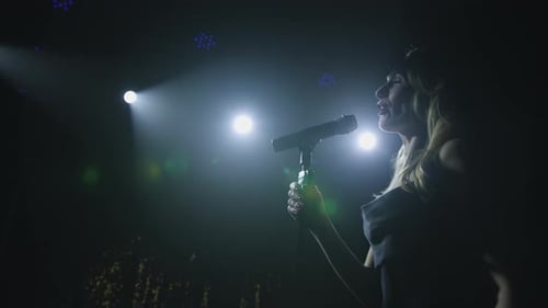 Close-up of the Face of the Singer with Microphone on a Black Smoky Background. The Singer Sings a