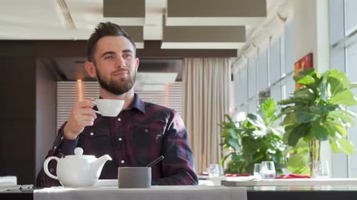 Bel homme barbu regardant loin pensivement, profitant du thé du matin