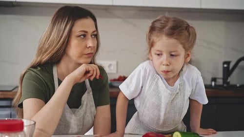 Mother and Daughter Eat Red Bell Pepper at Table in Kitchen